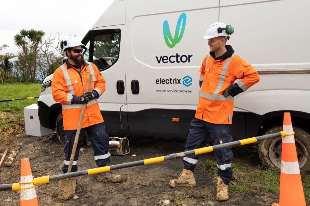 two workers standing by vector branded vehicles on work site