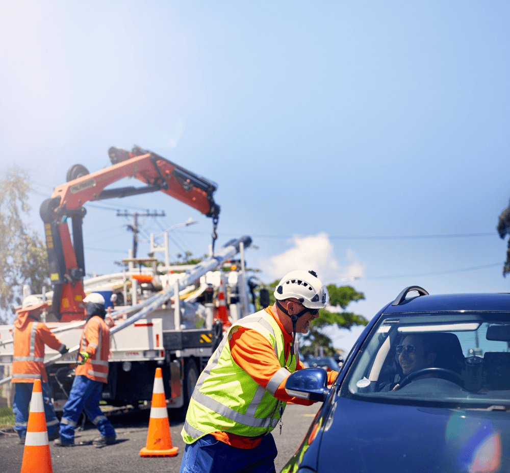 Crew member talking to a customer in car with background of electricity network work going on